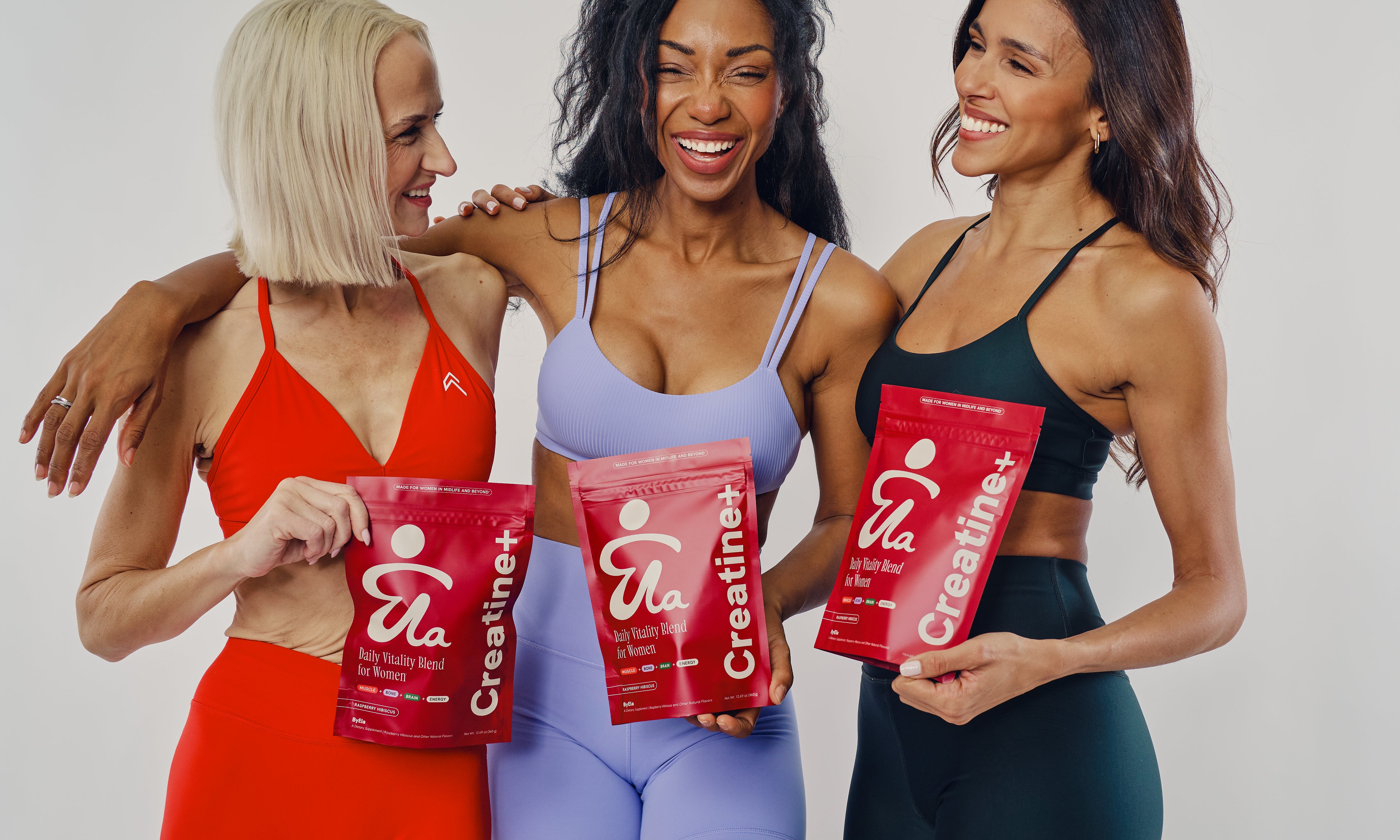 Three women in activewear holding ByEla Creatine+ pouches together, representing community, shared strength, and midlife support.