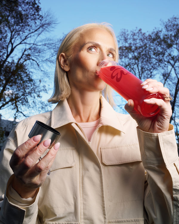 Midlife woman outdoors drinking a red ByEla supplement, supporting cognitive clarity and daily vitality